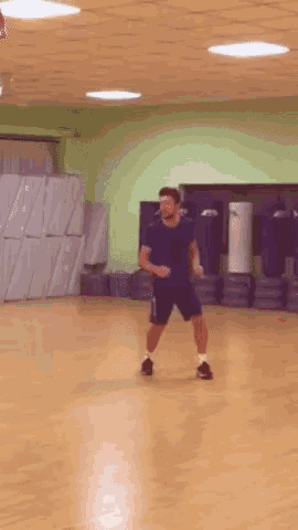 a man in a black shirt and shorts is standing on a wooden floor