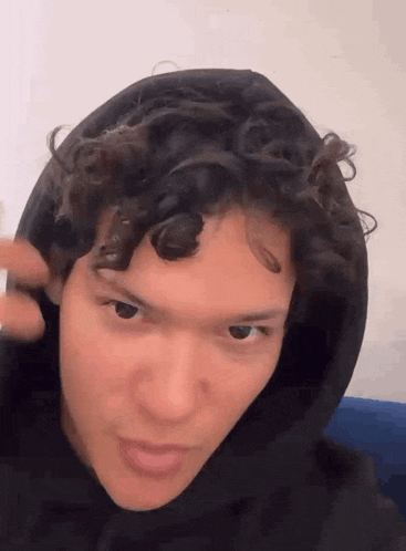 a young man with curly hair is wearing a black hoodie .