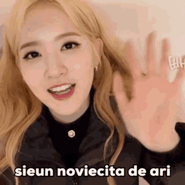 a girl with blonde hair is smiling and waving her hand with the words sieun noviecita de ari written below her