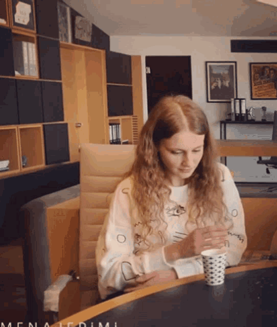 a woman sits at a table with a cup of coffee in front of her and a sign that says menagerie