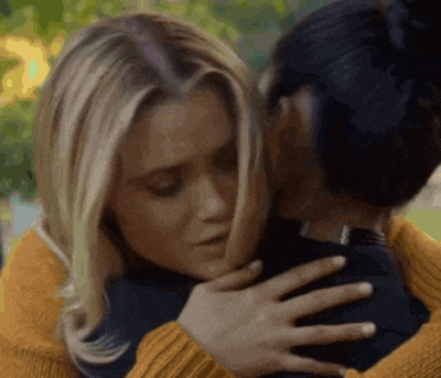 two women are hugging each other in a park . one of the women is wearing a yellow sweater .