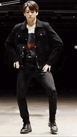a young man in a black jacket and black pants is standing on one leg .