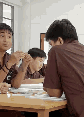 a man wearing a brown shirt with the letter c on it sits at a table with other people