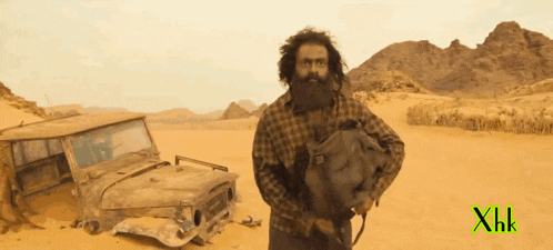 a man with a beard is standing in the desert next to a jeep with the letters xhk on the bottom