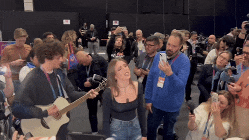 a woman singing while a man plays a guitar in front of a crowd of people