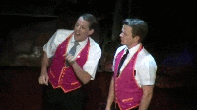 two men are standing next to each other on a stage wearing pink vests .