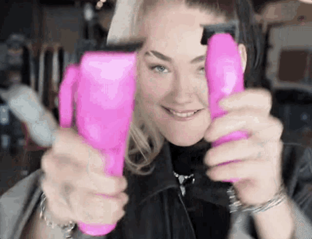 a woman is smiling while holding two pink hair clippers in her hands .