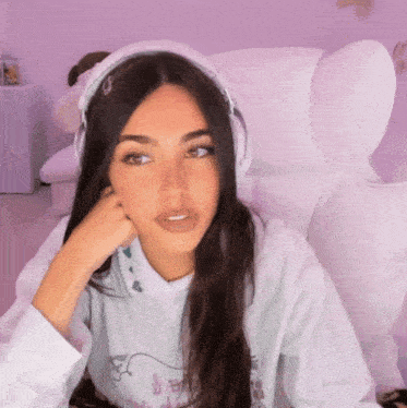 a woman wearing headphones and a hoodie is sitting in a white chair .