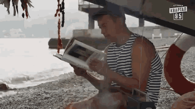 a man reading a book on a beach with a sign that says ' квартира 1951 ' on it