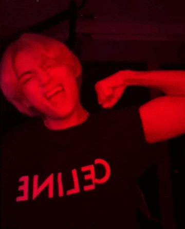 a man wearing a black shirt with the word celine on it is dancing in a dark room with red lights .