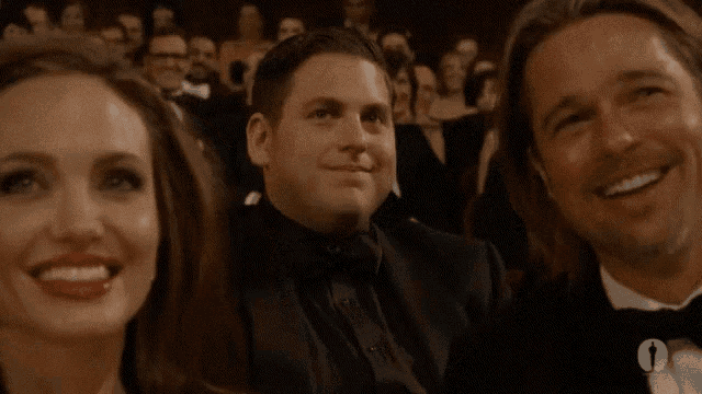 a man in a tuxedo is smiling while sitting next to a woman and another man