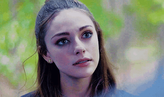 a close up of a woman 's face with blue eyes and a ponytail .