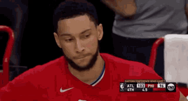 a man in a red shirt is sitting in the stands watching a game