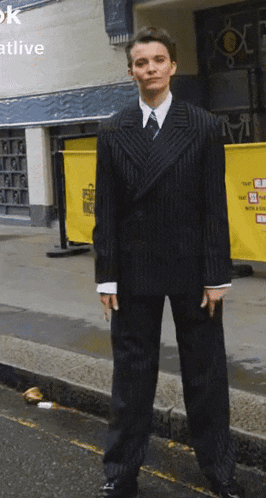 a man in a suit and tie is standing on a sidewalk in front of a building that says ok at live