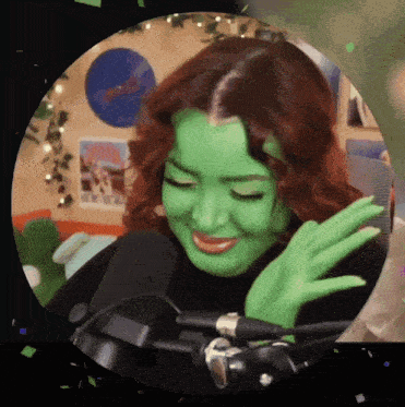 a woman with green paint on her face is smiling while standing in front of a microphone