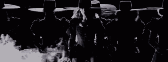 a group of men in hats are standing in a dark room with smoke coming out of them .