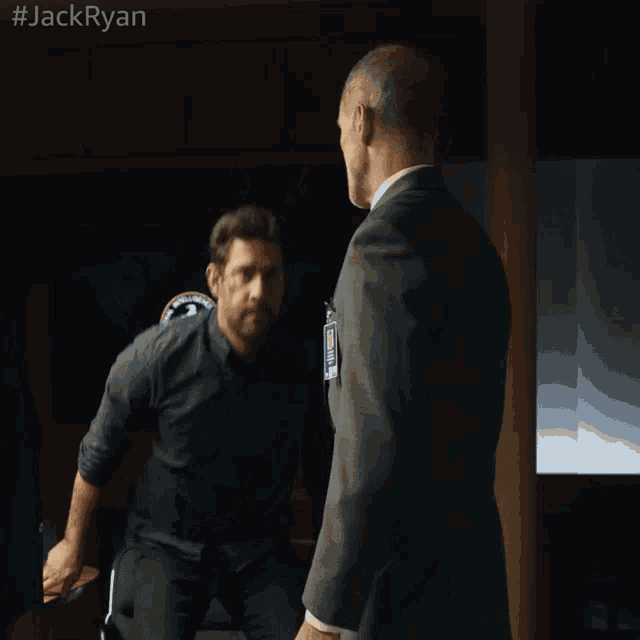 two men shaking hands in a dark room with the hashtag #jackryan