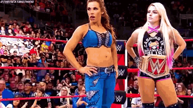 two female wrestlers are standing in a wrestling ring with their hands on their hips .