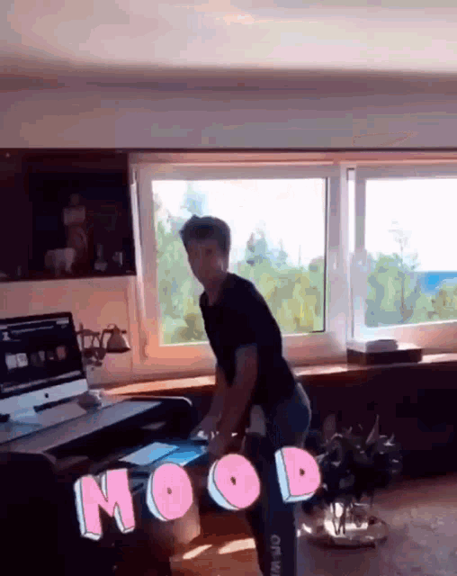 a man in a black shirt is standing in front of a window with the word mood on the floor