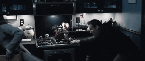a man is reaching for something on a stove top in a kitchen
