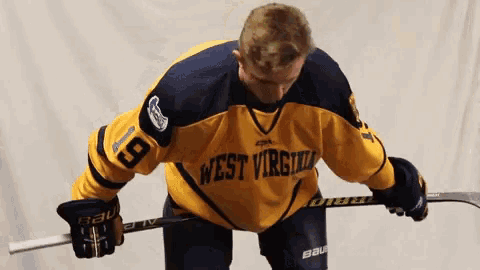 a hockey player wearing a west virginia jersey is holding a stick