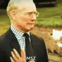 a man in a suit and tie is making a funny face and holding his hand to his chest .