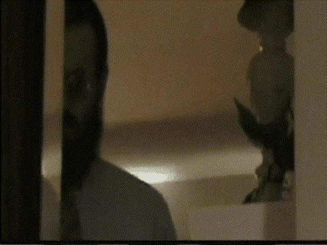 a man is standing in front of a mirror in a dark room looking at himself .