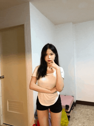 a woman standing in a room with her arms crossed and a pink suitcase behind her