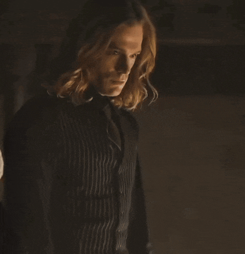 a man with long hair is standing in a dark room with a blurred background .
