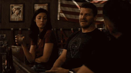 a man and a woman are sitting at a bar with an american flag in the background