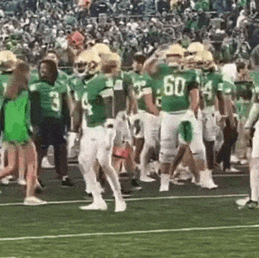 a group of football players in green uniforms are walking on the field .