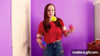 a girl in a red crop top is holding a tennis ball in her mouth in front of a purple wall .