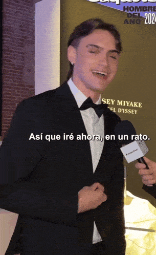 a man in a suit and bow tie is talking into a microphone and says así que