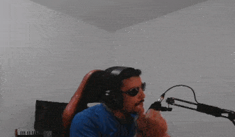 a man wearing headphones and sunglasses is sitting in front of a microphone in a room .