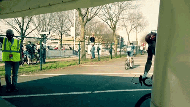 a man wearing a yellow vest is talking on a cell phone while a man on a bike rides by