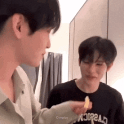 two young men are standing next to each other in a room and one of them is holding a piece of food .