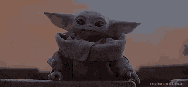 a baby yoda from star wars is sitting on a ledge looking at the camera .
