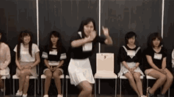 a group of young women are sitting in chairs and a woman is dancing in front of them .