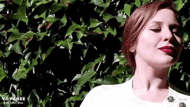 a woman with red hair is standing in front of a bush with the word voyager on the bottom
