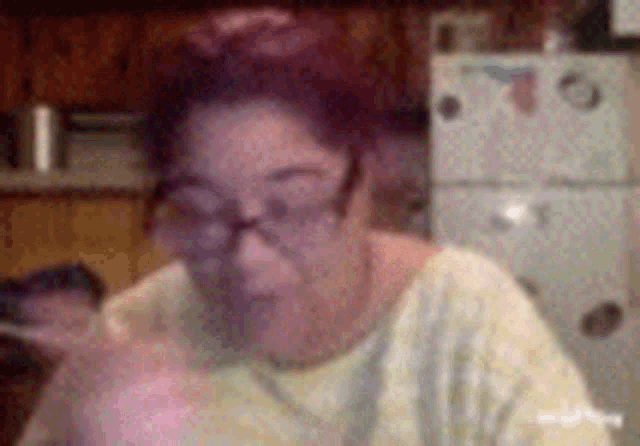a woman wearing glasses and a yellow shirt is sitting in front of a refrigerator in a kitchen .
