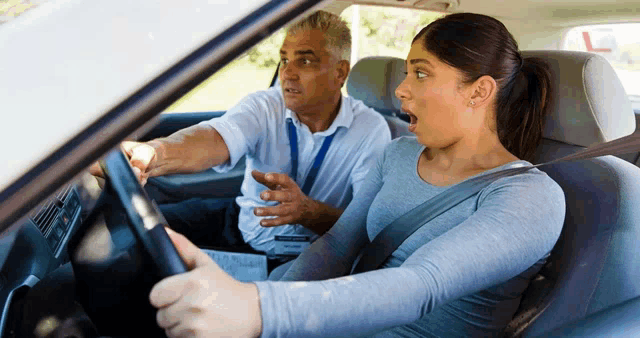 a woman is sitting in a car with a driving instructor behind her