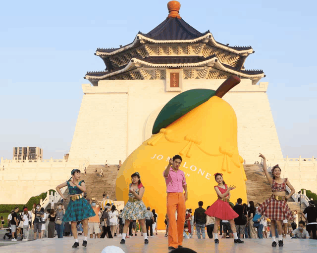 a group of people are dancing in front of a large yellow pear that says jo lone on it