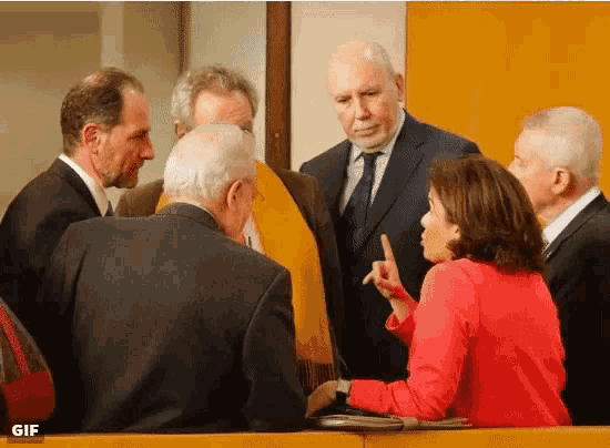 a woman in a red sweater is talking to a group of men in suits