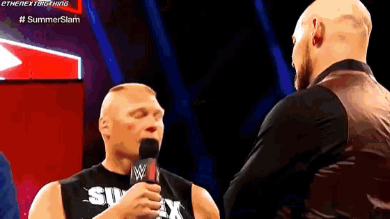 brock lesnar is talking into a microphone while standing next to another man .