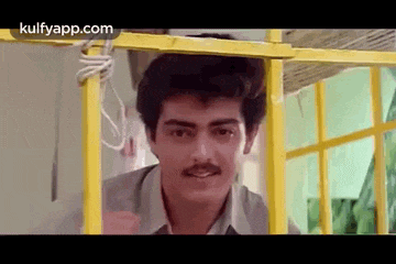 a man with a mustache is looking out of a yellow cage .