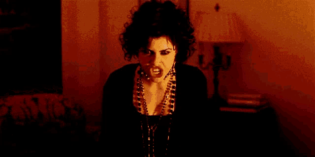 a woman with curly hair is sitting on a couch in a dark room with a lamp in the background .