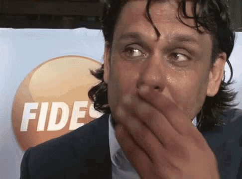 a man covering his mouth with his hand in front of an ad for fides