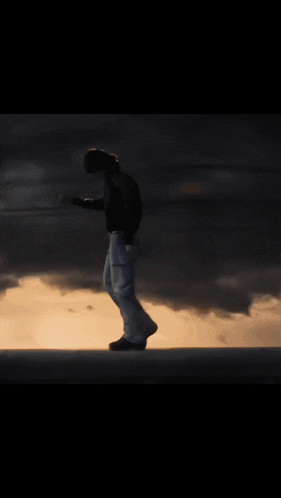 a man in a black jacket and white pants is walking in the dark