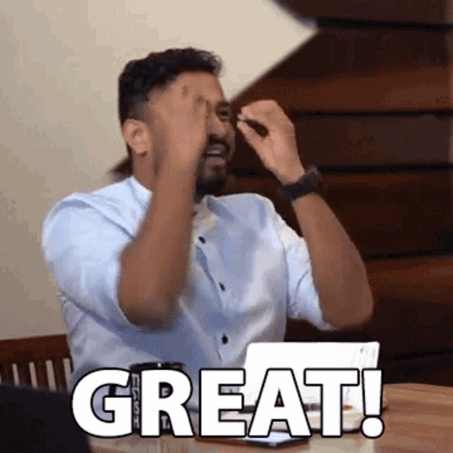 a man is sitting at a table with a laptop and a cup of coffee and says great .
