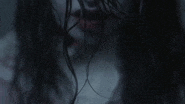 a close up of a woman 's face with long black hair and blood coming out of her mouth .